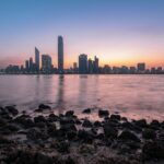 Stunning Abu Dhabi cityscape at sunrise with calm ocean foreground and vibrant sky.