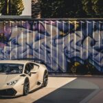 A sleek luxury sports car parked in front of a vibrant graffiti wall under bright daylight.