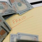 Close-up of US dollars and 'Fraud' written on yellow paper, representing financial scams.