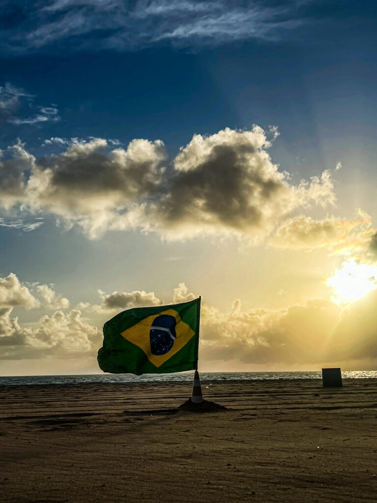 A vibrant Brazilian flag flutters by the seaside during a stunning sunrise in João Pessoa, Brazil.